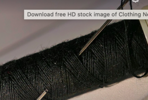 A spool of black thread with sewing needles pushed into it